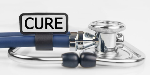 On the white surface lies a stethoscope with a plate with the inscription - CURE