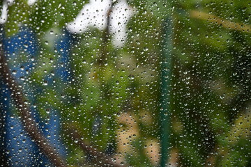 Transparent glass window surface covered with shiny raindrops from behind and shot inside car. Defocus texture of water drops with copy space