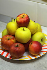 A heap of apples in a plate on the table. Red and green juicy ripe apples lie in a slide on a white plate against the background of a gray wall. Stock photography fruit top view