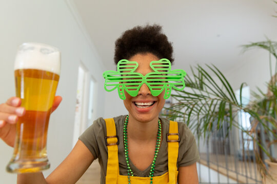 Mixed race woman celebrating st patrick's day making video call holding a beer - Powered by Adobe