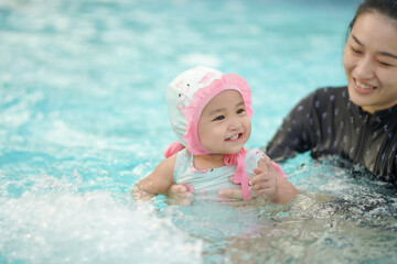 Fototapeta na wymiar Asian cute baby girl in swimsuit holding by her young mother enjoying in the swimming pool with copy space