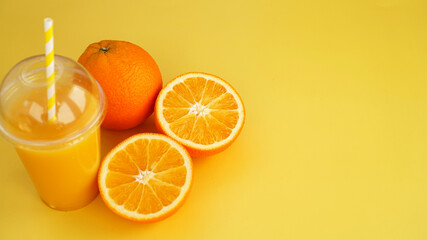 Orange juice in a plastic glass with a straw. Sliced orange on a yellow