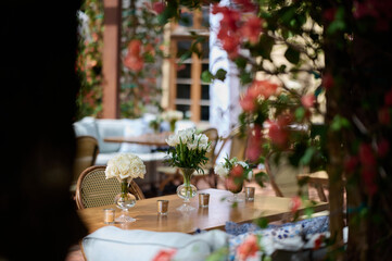 Focus on the table setting with vases with white flowers and candles, red flowers on the foreground