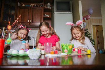 Three girls coloring Easter eggs at home at the kitchen table