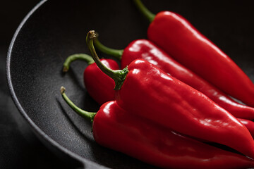 Red peppers in a black pan on a black background. Horizontal shot