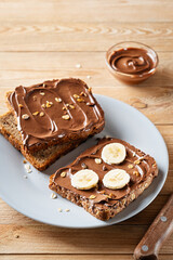 Fresh toasts with chocolate spread and slices of banana on a gray plate on a wooden background