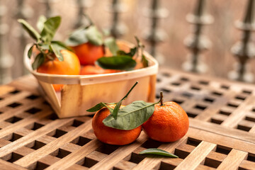 Basket of tangerines with leaves on wooden table, selective blur