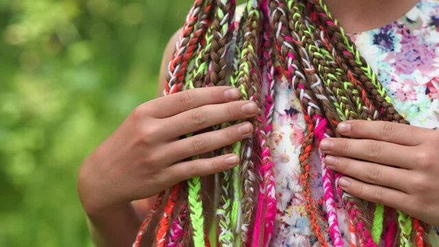 A teenage girl is touching her multi-colored dreadlocks.