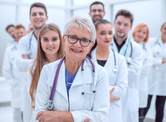 elderly woman doctor standing in front of a team of her young colleagues.