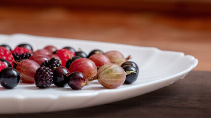 Assorted berries of raspberries, gooseberries, currants on a white plate