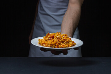 Italian pasta on a dark background. The chef serves food on a black background. Home traditional cuisine.