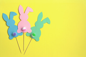 Colorful paper Easter bunnies on a yellow background. Easter bunnies on a stick with fluffy tails. Easter and creative concept.