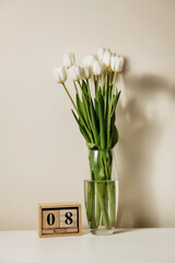 White fresh beautiful tulips in a transparent glass vase for women's holiday on march 8, isolated on a light background