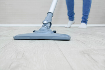 Handheld gray vacuum cleaner close-up and woman's legs. Vacuum the floor in room.