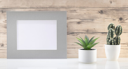 Modèle de cadre photo blanc avec espace vide pour logos, inscription publicitaire. Cadre en mode paysage sur un espace de travail avec des plantes vertes. Ambiance zen.	