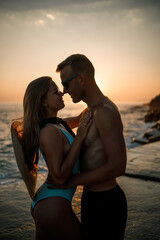 Beautiful couple in love on the background of the sunset by the sea. Young woman and man hugging by the sea at sunset