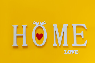 Home, wooden text with heart shape decor on yellow background. Concept of building houses, choosing your house, mortgage, buying, selling residential area, rental, insurance, investment real estate.