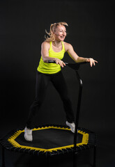 Girl on a fitness trampoline on a black background in a yellow t-shirt trampoline gym active exercise caucasian girl vitality, workout rebounder. Wellness white aerobics, physical muscle instructor