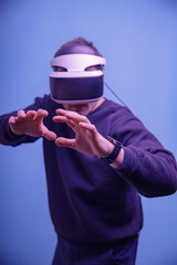 A man in his thirties wearing virtual reality glasses, playing video games with a virtual reality headset, tries to touch something with his hands.