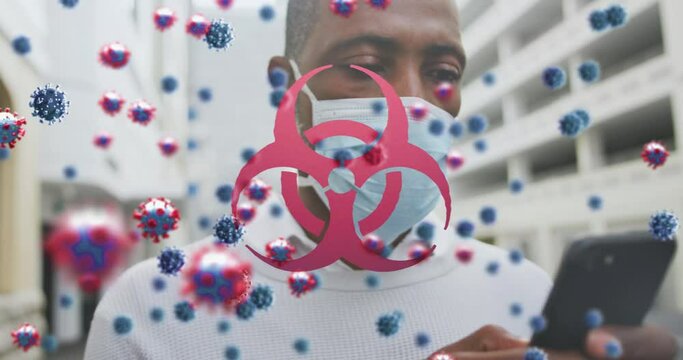 Animation of covid 19 cells and biohazard symbol over man in face mask using smartphone