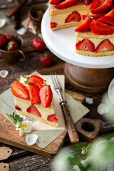 tasty homemade strawberry cake fraisier with biscuits and lot of white cream on wooden cake stand on rustic table with flowers, vintage forks, copper cups