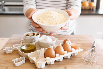 Woman holds a white bowl with chickpea flour over table with ingredients for gluten free cookies.Homemade healthy eating