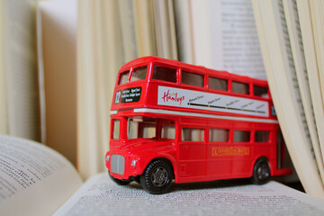 London red toy bus coming out of a book driving over a book