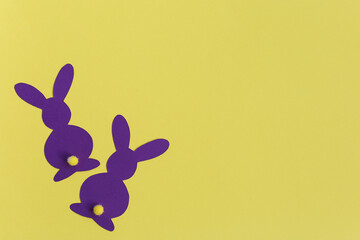 Two purple paper Easter bunnies on a yellow background. Creativity concept. Easter decor.