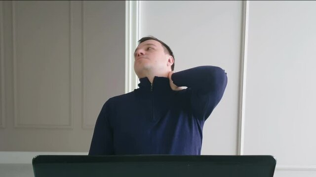 freelancer stretches, doing light  exercises to relieve muscle tension from sedentary work, middle age man stretching arms, relaxing neck, prevention of computer office syndrome concept