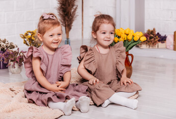 Two little girls in identical dresses sit on the floor with flowers