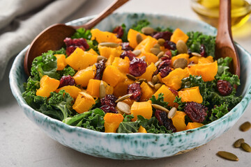 Fall salad with kale, roasted pumpkin, seeds and dried cranberries in bowl. Grey background. Mock up. Top view.