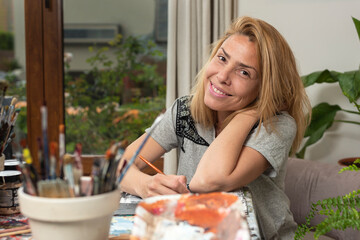 young latin woman plastic artist painter very happy in her art studio with her canvases and brushes