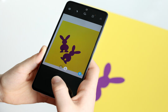 Photo on phone layouts of two purple paper Easter bunnies on a yellow background. Creativity concept. Easter decor.