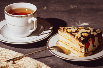 Still life - layered homemade sponge cake and a cup of black tea in a white dish, and a linen napkin, black background, hard light, photo in a low key.