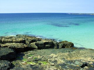 Landscape in Scotland (Outer Hebrides): rocky shore, clear bright blue water, white sand and bright blue sky, an idyllic summer day scene.