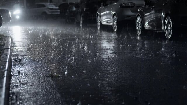 Pouring rain in the dark city yard at night. Selective focus on the asphalt road with raindrops. Static camera