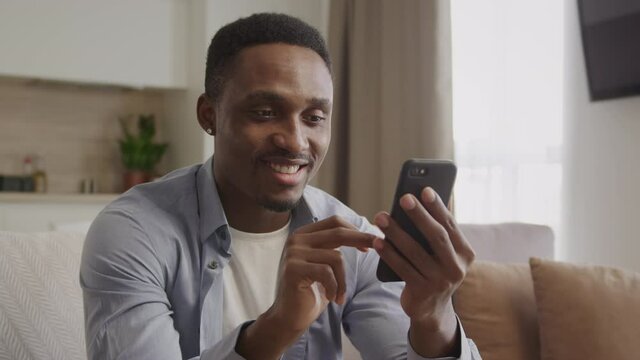A bunch of various facial expressions by an adult african american man browsing the web on a black smart phone indoors