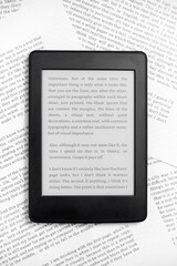 Fototapeta premium Electronic reader with the screen on and a text on it, on paper sheets.