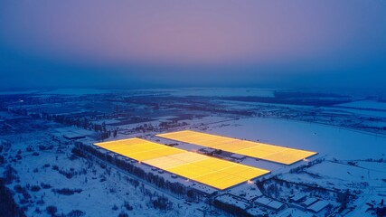 Aerial side view of large industrial greenhouses for growing plants in winter. light pollution. winter day at sunset. Flying along modern plantation glasshouse area. growing plants vegetables flowers