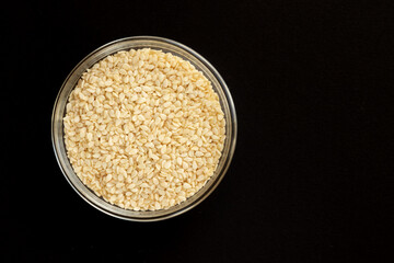 Sesame seeds in a glass bowl, isolated on black background. Top view.