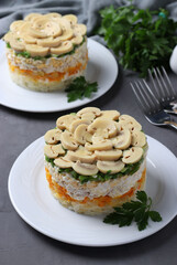Two servings of puff salad with chicken, pickled mushrooms, potatoes and carrots on plates. Closeup
