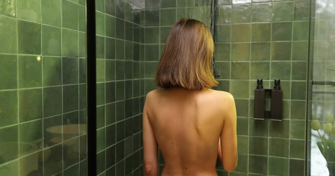 Young woman with brown hair showering in the green bathroom, standing back under the rain shower