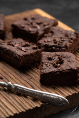 Dark brownies with choco drops on ribbed oak wood cutboard on dark concrete background