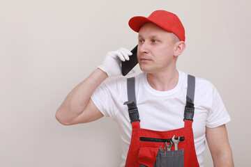 construction male worker In red working form and cap with cellphone in hand and communicates with customers isolated on white background. of the service delivery is a career