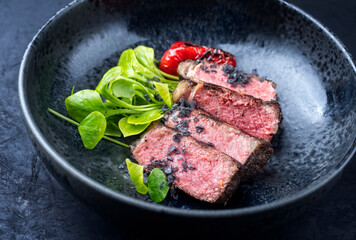 Modern style traditional dry aged sliced wagyu roast beef with fried onion rings served as close-up on a rustic black board