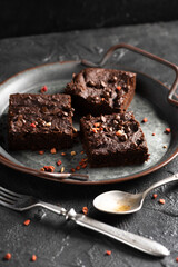 Dark cacao brownies with choco drops on old metal tray with vintage silverware on dark concrete background