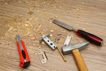 Shavings on floor from door latch installing. Wood sawdust from hole for door lock making. Hammer, chisel, knife, screws, pencil and latch on floor.