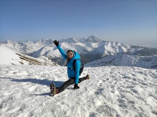 A woman tourist is doing splits on the top of the mountain. Beautiful winter mountain landscape.