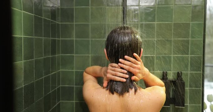 Young woman with brown hair showering in the green bathroom, standing back under the rain shower
