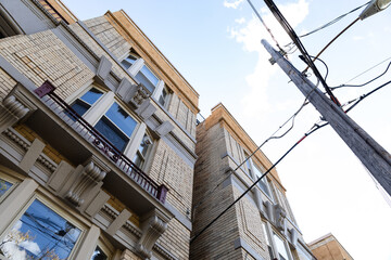 Extreme upward view of old light brick apartment buildings with power pole and lines, horizontal aspect